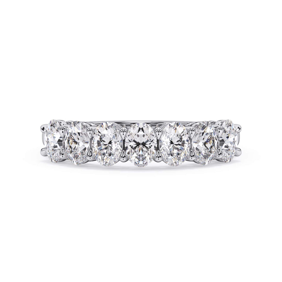 A picture of a seven stone diamond wedding ring with oval shaped diamonds that are shared prong set in white gold or platinum on a white background with the ring facing forward, lying down.