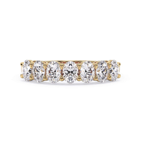 A picture of a seven stone diamond wedding ring with oval shaped diamonds that are shared prong set in yellow gold on a white background with the ring facing forward, lying down.