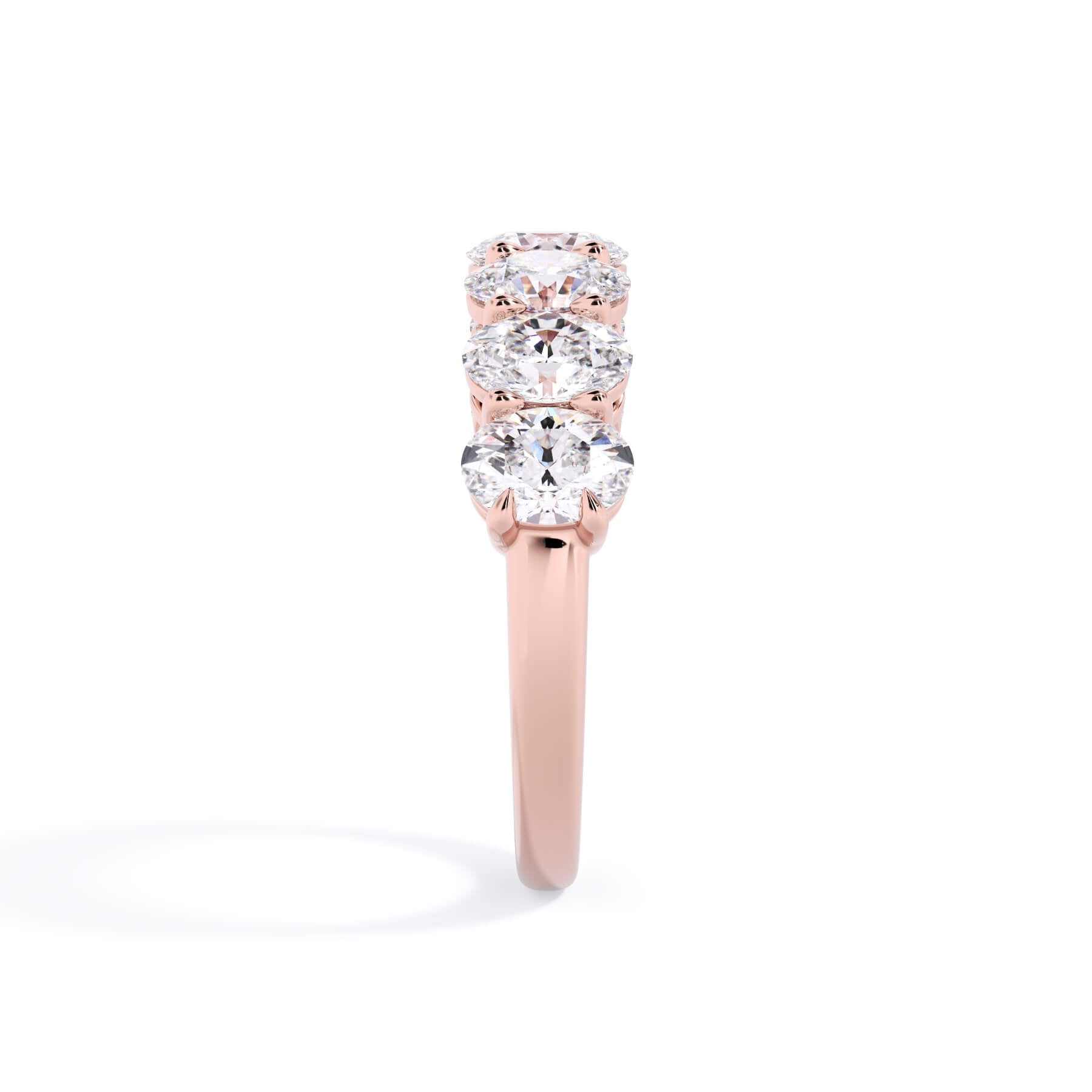 A picture of a seven stone diamond wedding ring with oval shaped diamonds that are shared prong set in rose gold on a white background with a side profile view.