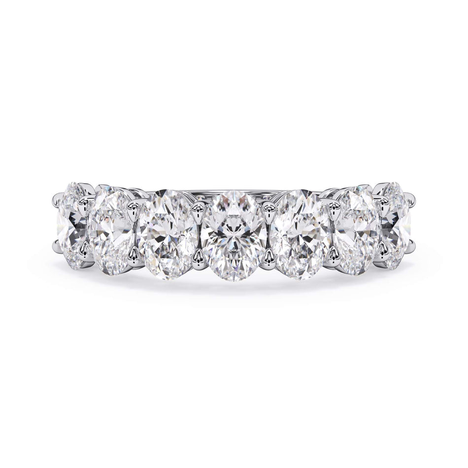 A picture of a seven stone diamond wedding ring with oval shaped diamonds that are shared prong set in white gold or platinum on a white background with the ring facing forward, lying down.