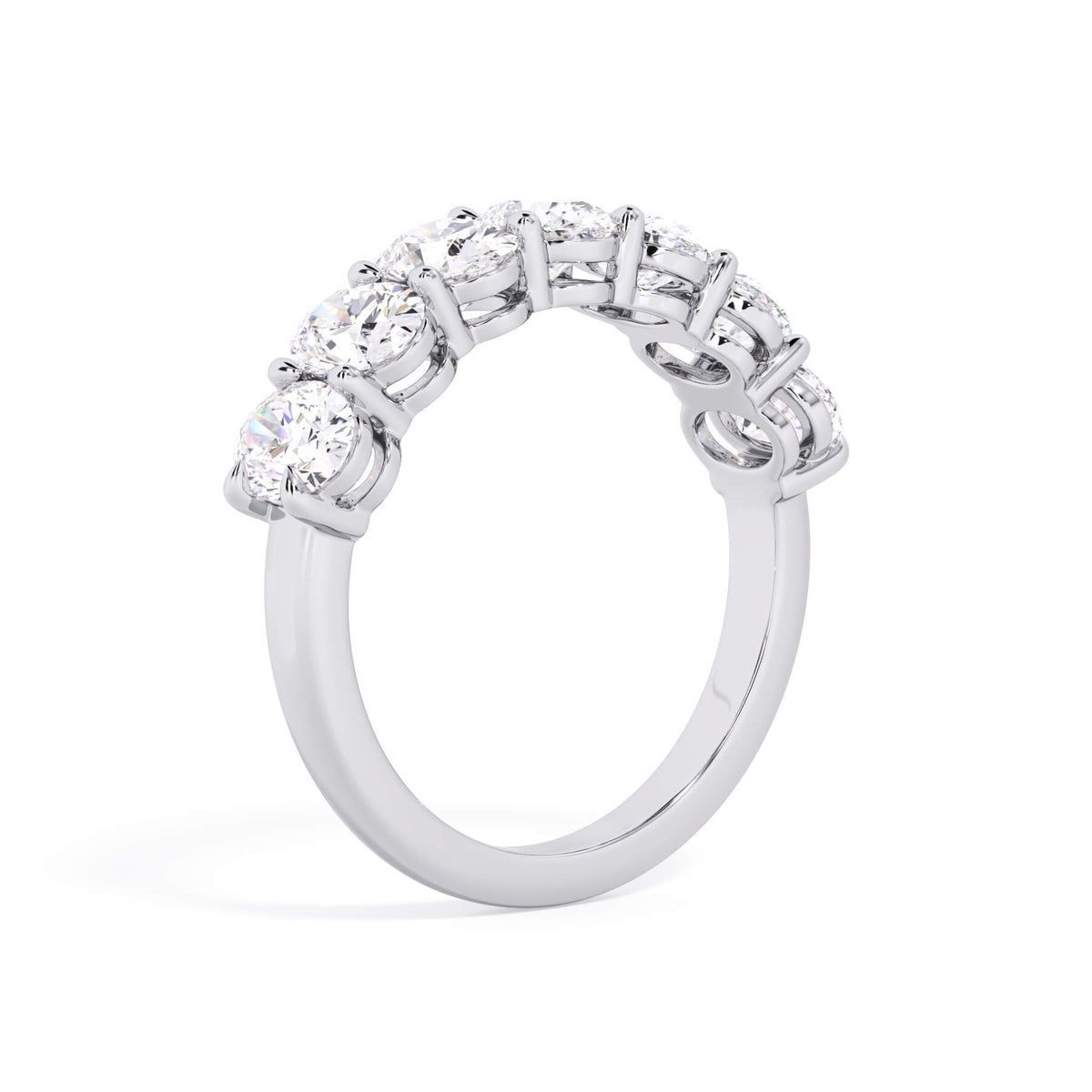 A picture of a seven stone diamond wedding ring with oval shaped diamonds that are shared prong set in white gold or platinum on a white background with a slightly angled, through the finger view.