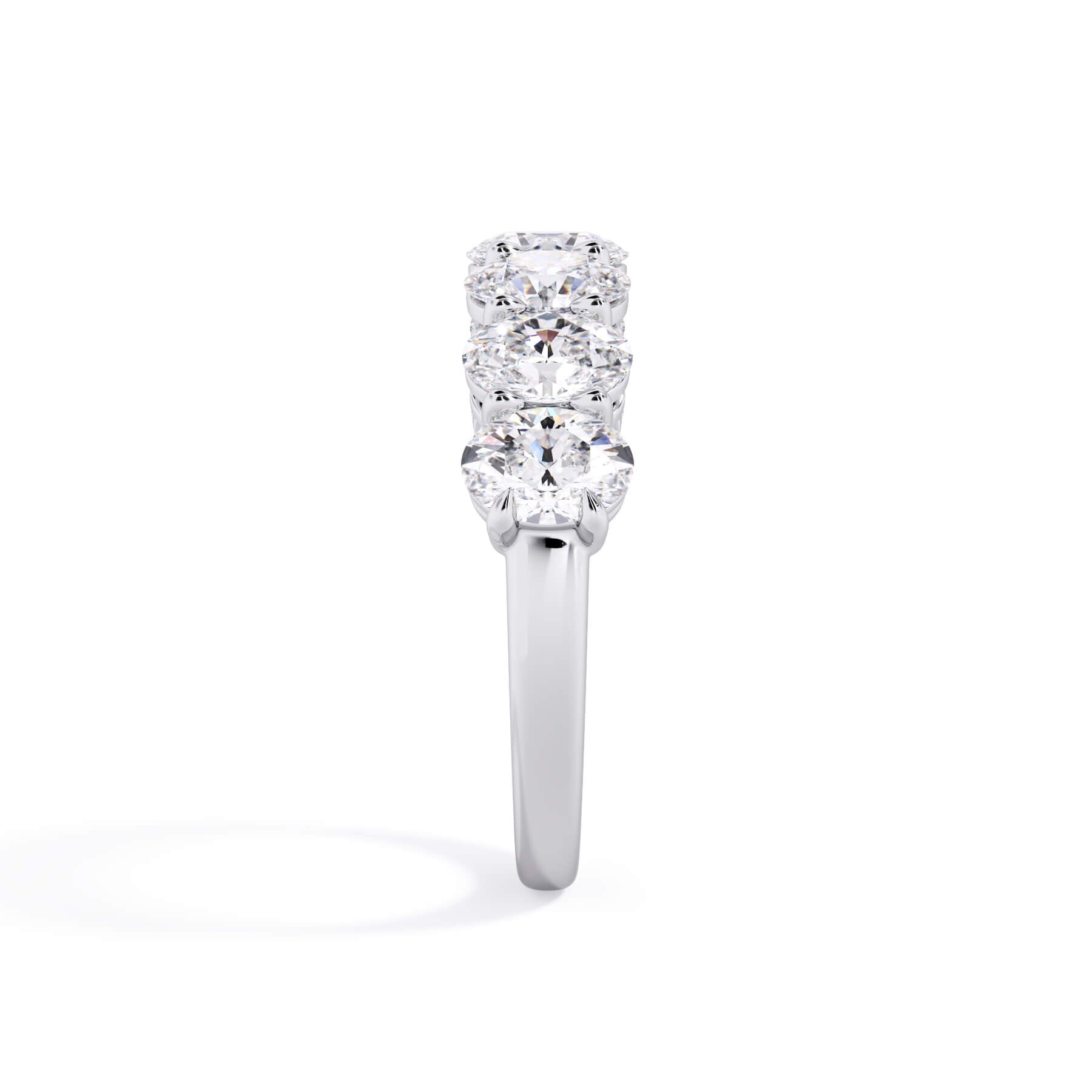 A picture of a seven stone diamond wedding ring with oval shaped diamonds that are shared prong set in white gold or platinum on a white background with a side profile view.