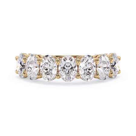 A picture of a seven stone diamond wedding ring with oval shaped diamonds that are shared prong set in yellow gold on a white background with the ring facing forward, lying down.