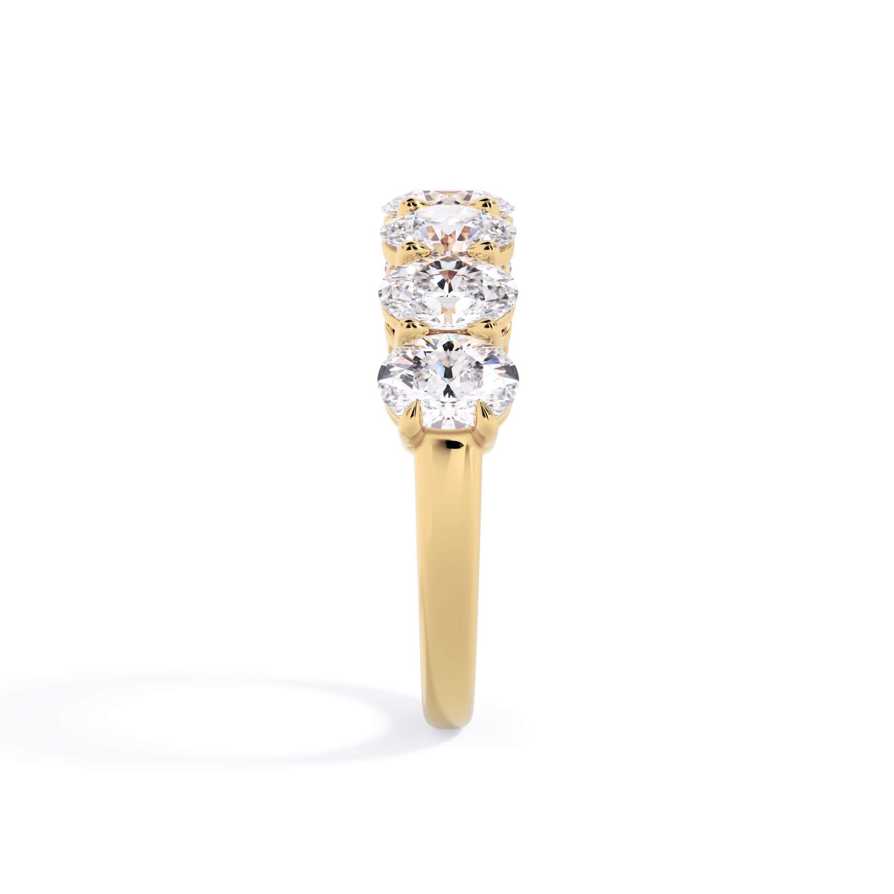 A picture of a seven stone diamond wedding ring with oval shaped diamonds that are shared prong set in yellow gold on a white background with a side profile view.