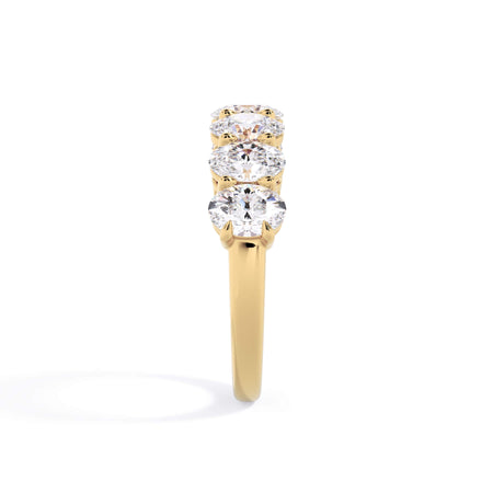 A picture of a seven stone diamond wedding ring with oval shaped diamonds that are shared prong set in yellow gold on a white background with a side profile view.