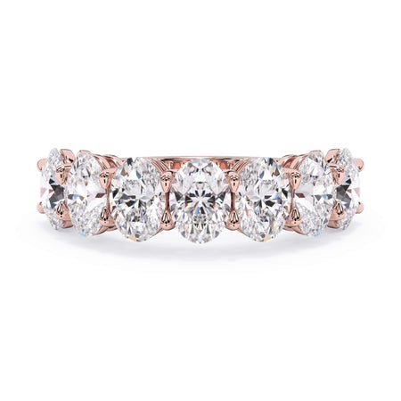 A picture of a seven stone diamond wedding ring with oval shaped diamonds that are shared prong set in rose gold on a white background with the ring facing forward, lying down.