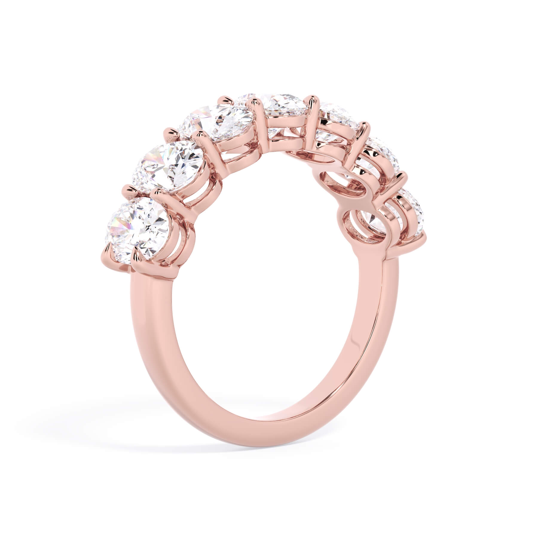 A picture of a seven stone diamond wedding ring with oval shaped diamonds that are shared prong set in rose gold on a white background with a slightly angled, through the finger view.