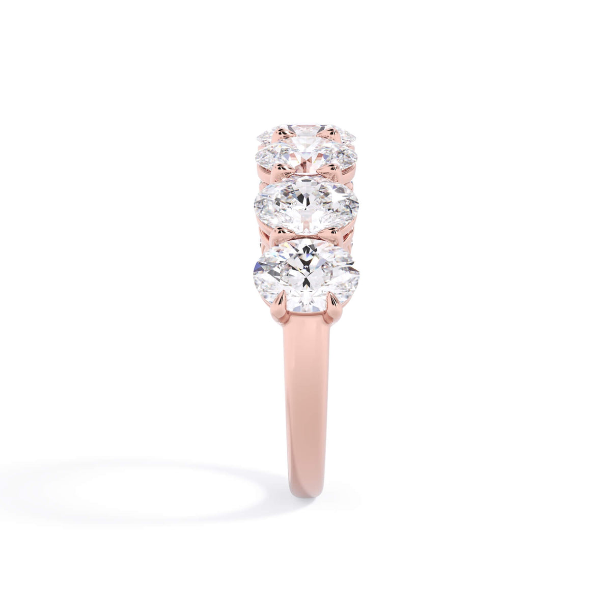 A picture of a seven stone diamond wedding ring with oval shaped diamonds that are shared prong set in rose gold on a white background with a side profile view.