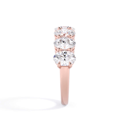 A picture of a seven stone diamond wedding ring with oval shaped diamonds that are shared prong set in rose gold on a white background with a side profile view.