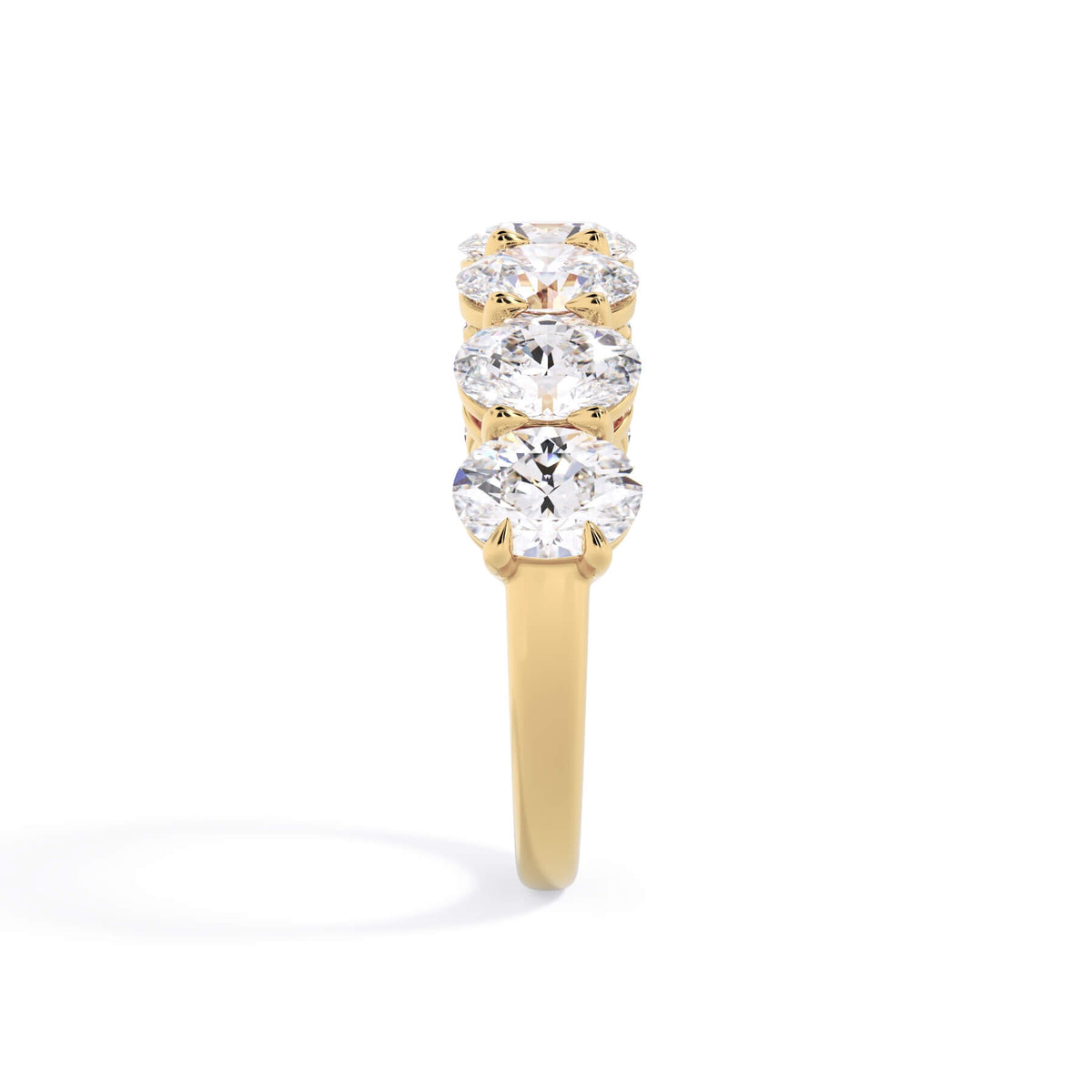 A picture of a seven stone diamond wedding ring with oval shaped diamonds that are shared prong set in yellow gold on a white background with a side profile view.