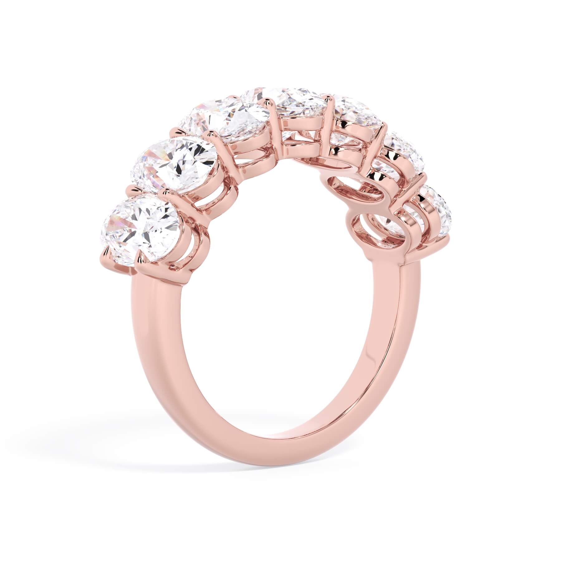 A picture of a seven stone diamond wedding ring with oval shaped diamonds that are shared prong set in rose gold on a white background with a slightly angled, through the finger view.