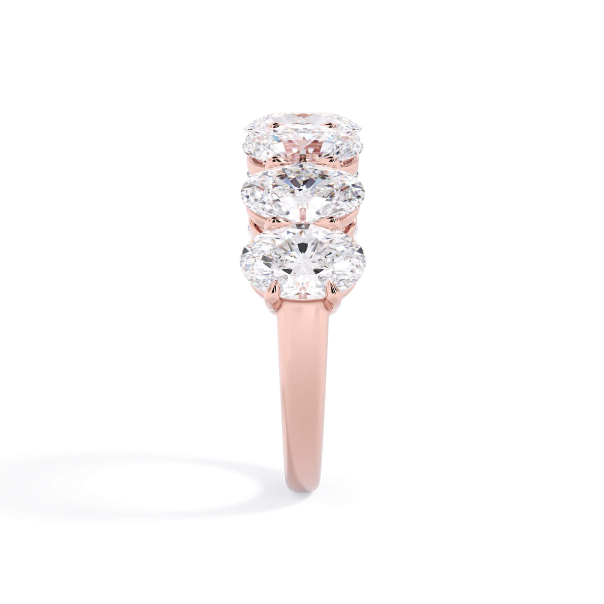 A picture of a seven stone diamond wedding ring with oval shaped diamonds that are shared prong set in rose gold on a white background with a side profile view.