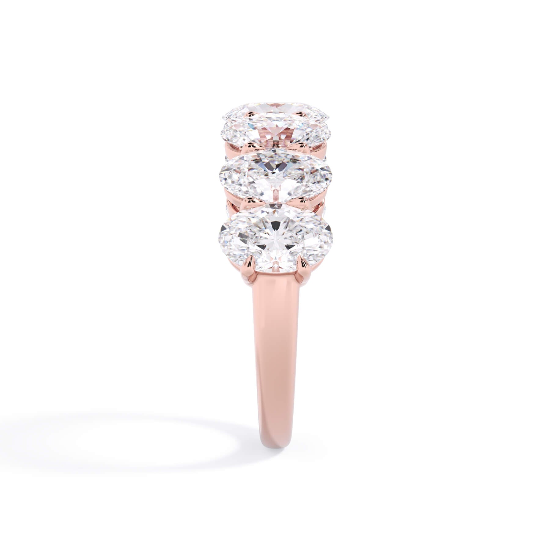 A picture of a seven stone diamond wedding ring with oval shaped diamonds that are shared prong set in rose gold on a white background with a side profile view.