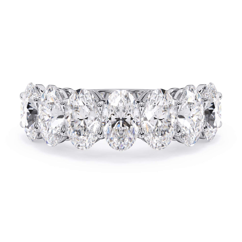 A picture of a seven stone diamond wedding ring with oval shaped diamonds that are shared prong set in white gold or platinum on a white background with the ring facing forward, lying down.