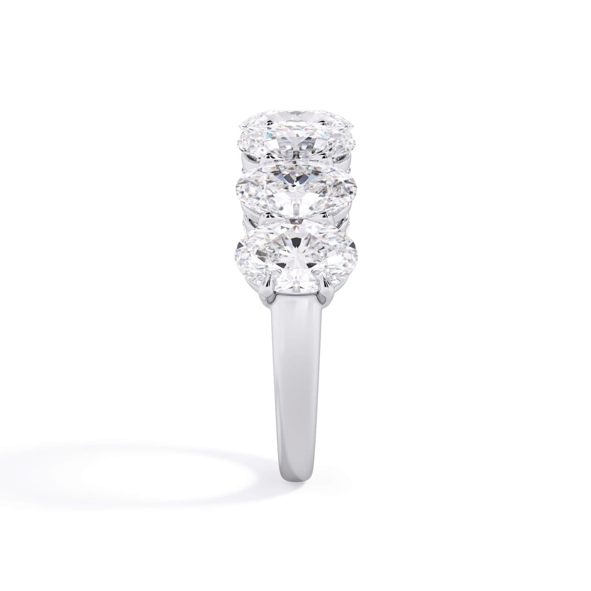 A picture of a seven stone diamond wedding ring with oval shaped diamonds that are shared prong set in white gold or platinum on a white background with a side profile view.