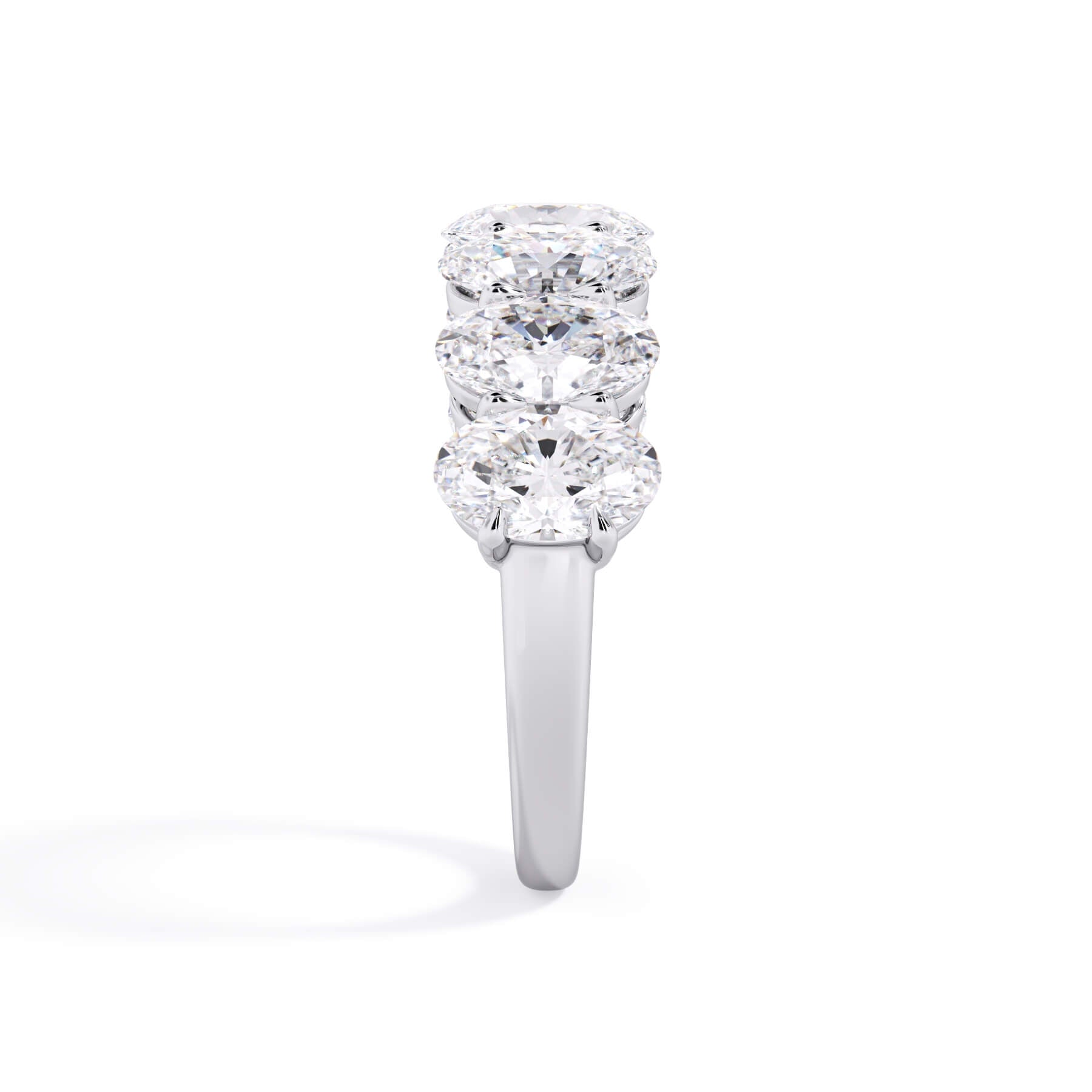 A picture of a seven stone diamond wedding ring with oval shaped diamonds that are shared prong set in white gold or platinum on a white background with a side profile view.