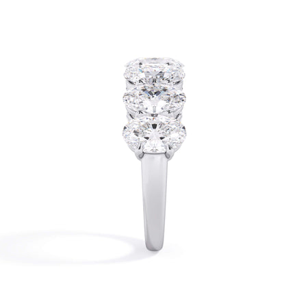 A picture of a seven stone diamond wedding ring with oval shaped diamonds that are shared prong set in white gold or platinum on a white background with a side profile view.