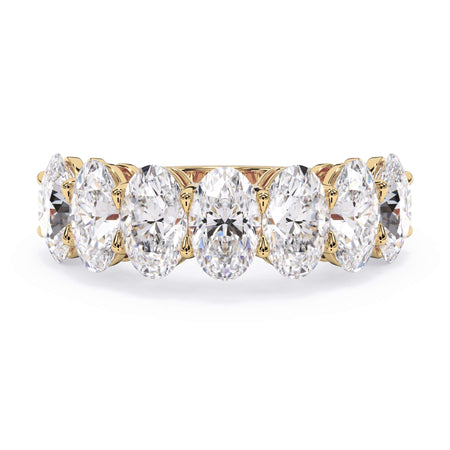 A picture of a seven stone diamond wedding ring with oval shaped diamonds that are shared prong set in yellow gold on a white background with the ring facing forward, lying down.