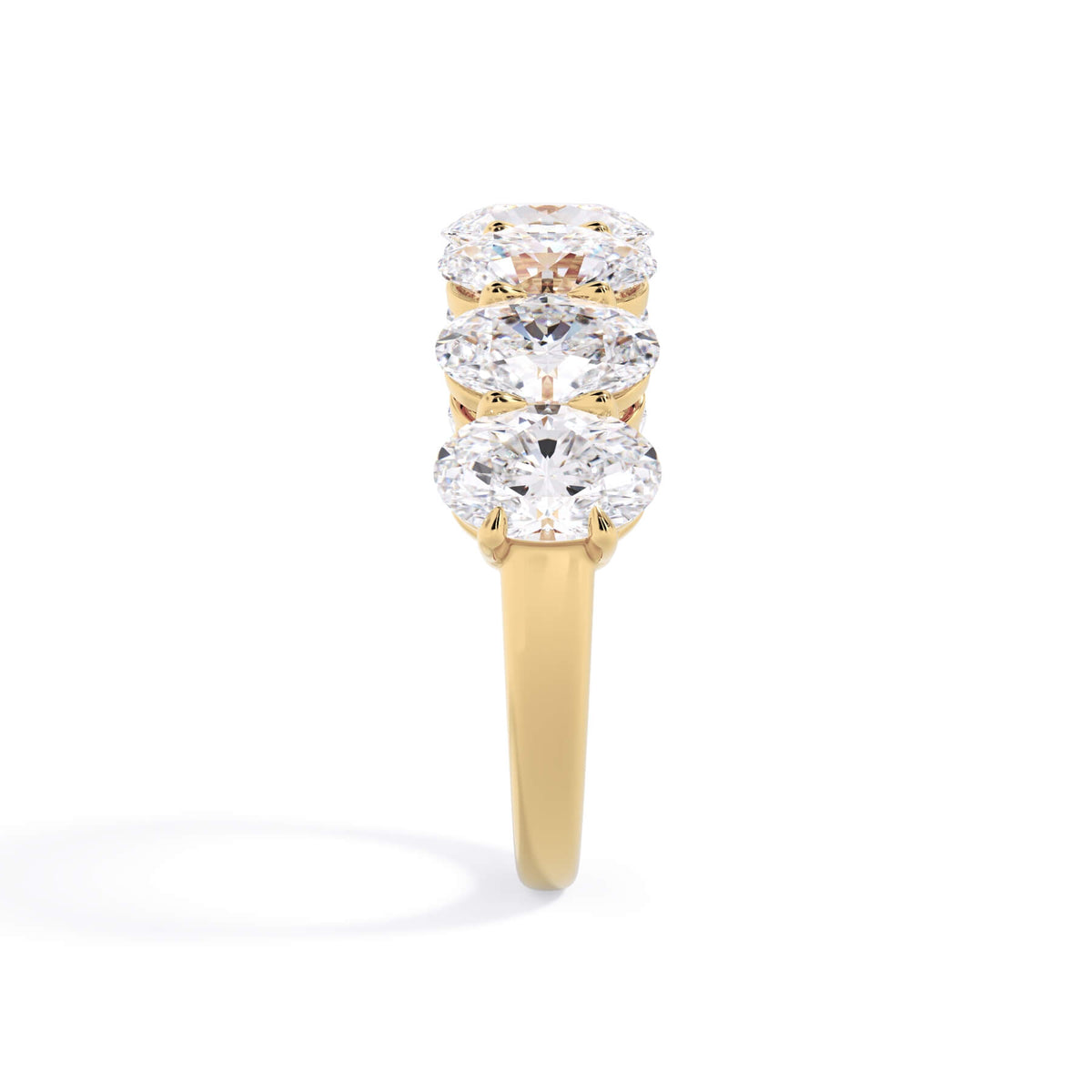 A picture of a seven stone diamond wedding ring with oval shaped diamonds that are shared prong set in yellow gold on a white background with a side profile view.
