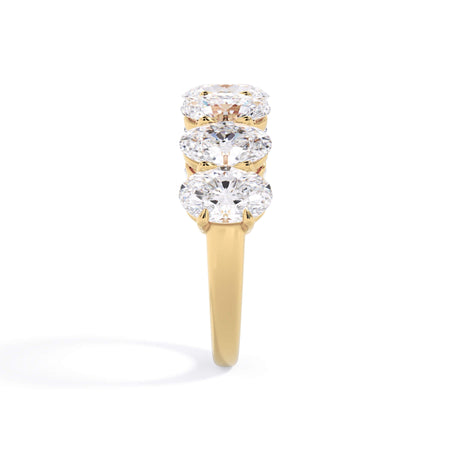 A picture of a seven stone diamond wedding ring with oval shaped diamonds that are shared prong set in yellow gold on a white background with a side profile view.