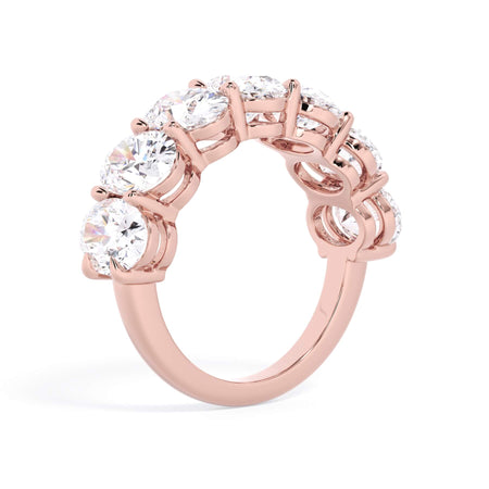 A picture of a seven stone diamond wedding ring with oval shaped diamonds that are shared prong set in rose gold on a white background with a slightly angled, through the finger view.