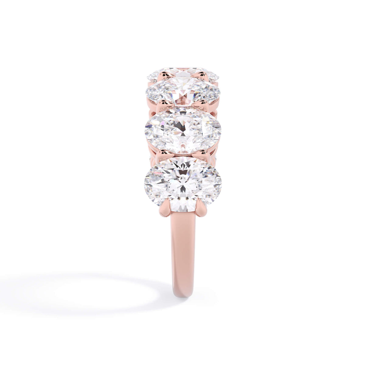 A picture of a seven stone diamond wedding ring with oval shaped diamonds that are shared prong set in rose gold on a white background with a side profile view.