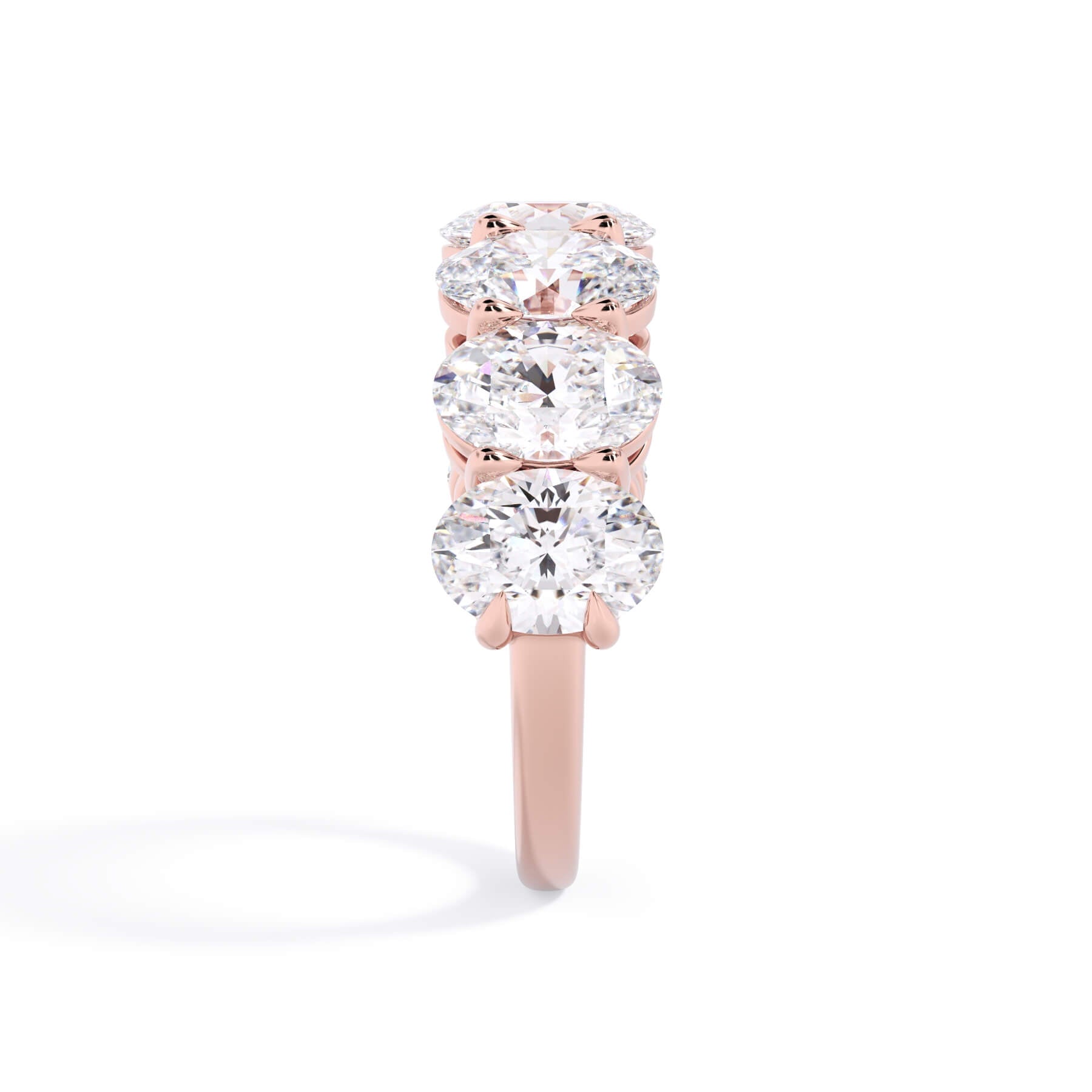 A picture of a seven stone diamond wedding ring with oval shaped diamonds that are shared prong set in rose gold on a white background with a side profile view.