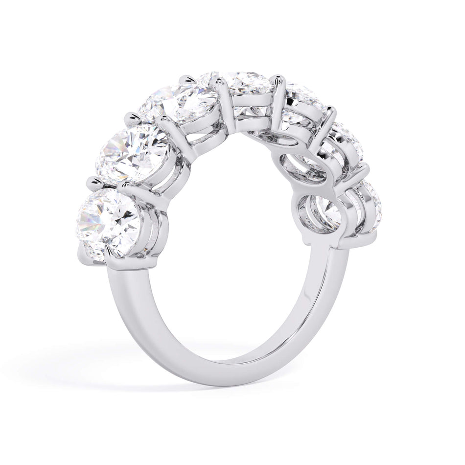 A picture of a seven stone diamond wedding ring with oval shaped diamonds that are shared prong set in white gold or platinum on a white background with a slightly angled, through the finger view.