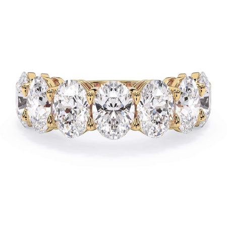 A picture of a seven stone diamond wedding ring with oval shaped diamonds that are shared prong set in yellow gold on a white background with the ring facing forward, lying down.