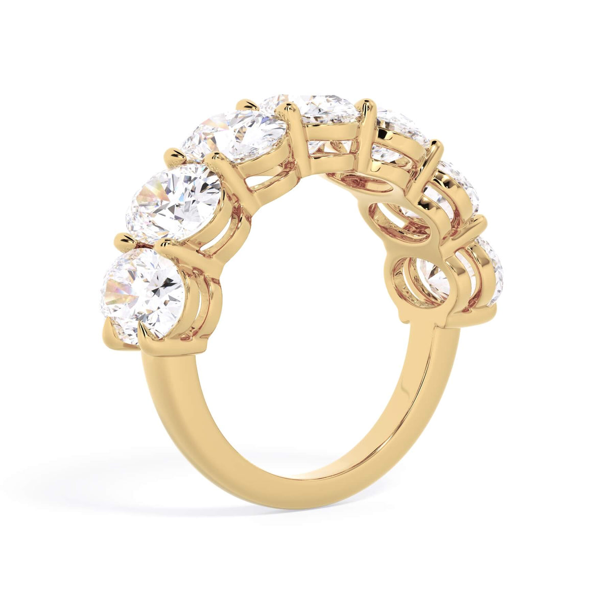 A picture of a seven stone diamond wedding ring with oval shaped diamonds that are shared prong set in yellow gold on a white background with a slightly angled, through the finger view.