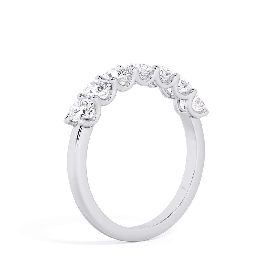 A picture of a seven stone diamond wedding ring with oval shaped diamonds that are U prong set in white gold or platinum on a white background with a slightly angled, through the finger view.