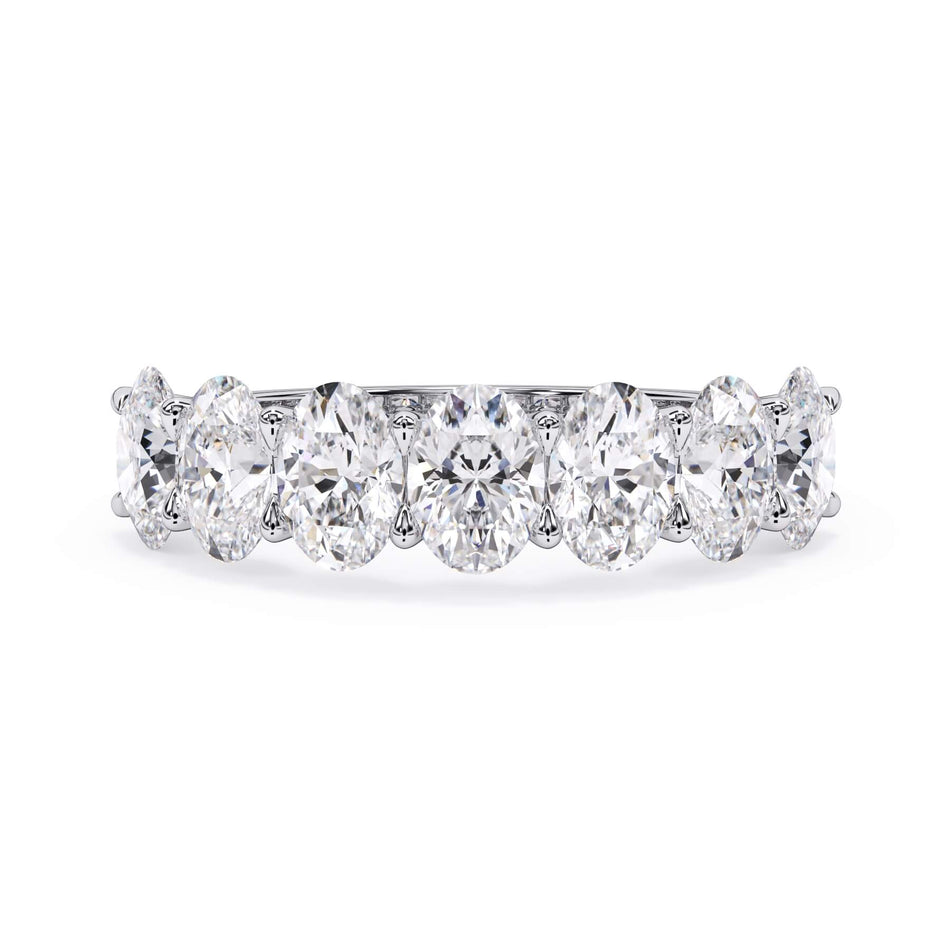 A picture of a seven stone diamond wedding ring with oval shaped diamonds that are U prong set in white gold or platinum on a white background with the ring facing forward, lying down.