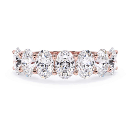 A picture of a seven stone diamond wedding ring with oval shaped diamonds that are U prong set in rose gold on a white background with the ring facing forward, lying down.