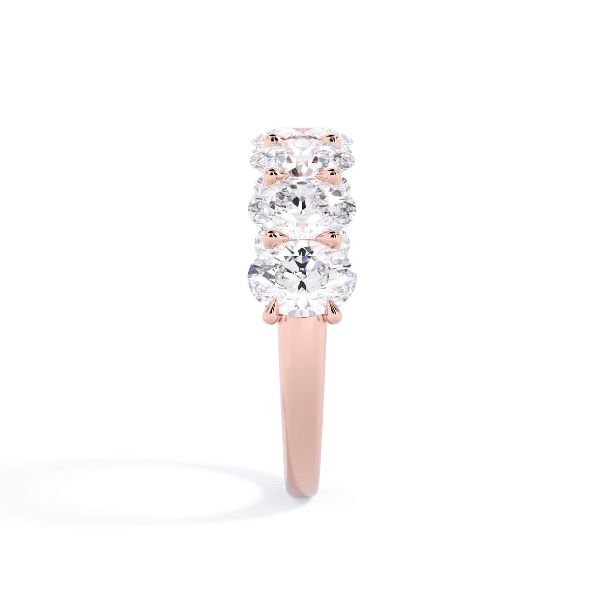 A picture of a seven stone diamond wedding ring with oval shaped diamonds that are U prong set in rose gold on a white background with a side profile view.