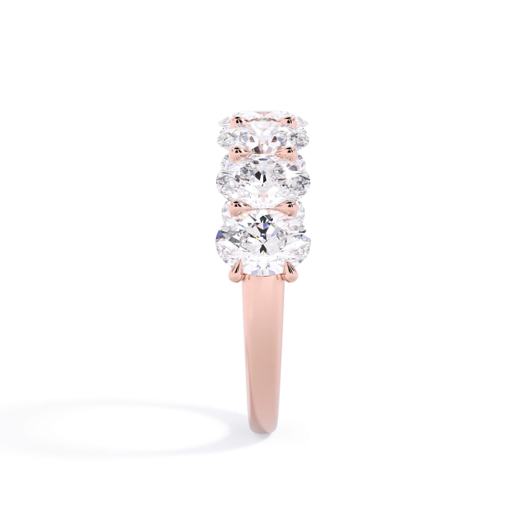 A picture of a seven stone diamond wedding ring with oval shaped diamonds that are U prong set in rose gold on a white background with a side profile view.