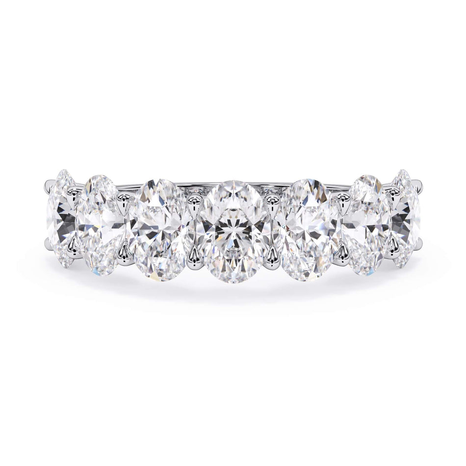 A picture of a seven stone diamond wedding ring with oval shaped diamonds that are U prong set in white gold or platinum on a white background with the ring facing forward, lying down.