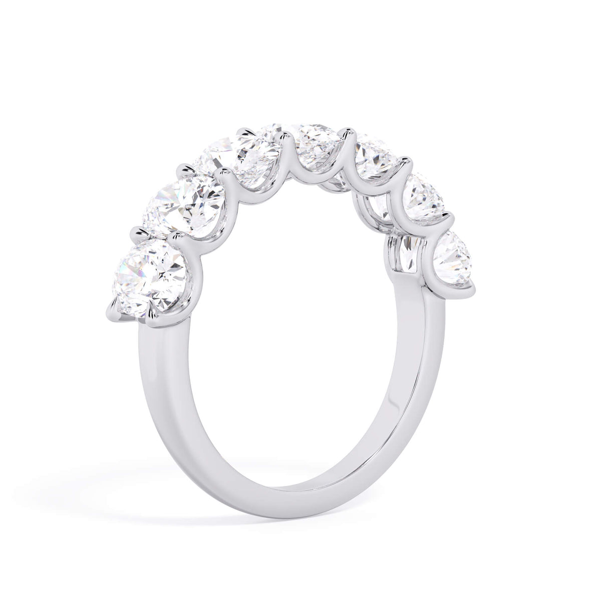 A picture of a seven stone diamond wedding ring with oval shaped diamonds that are U prong set in white gold or platinum on a white background with a slightly angled, through the finger view.