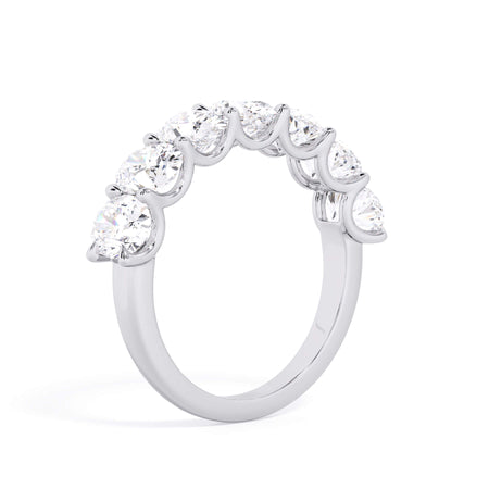 A picture of a seven stone diamond wedding ring with oval shaped diamonds that are U prong set in white gold or platinum on a white background with a slightly angled, through the finger view.