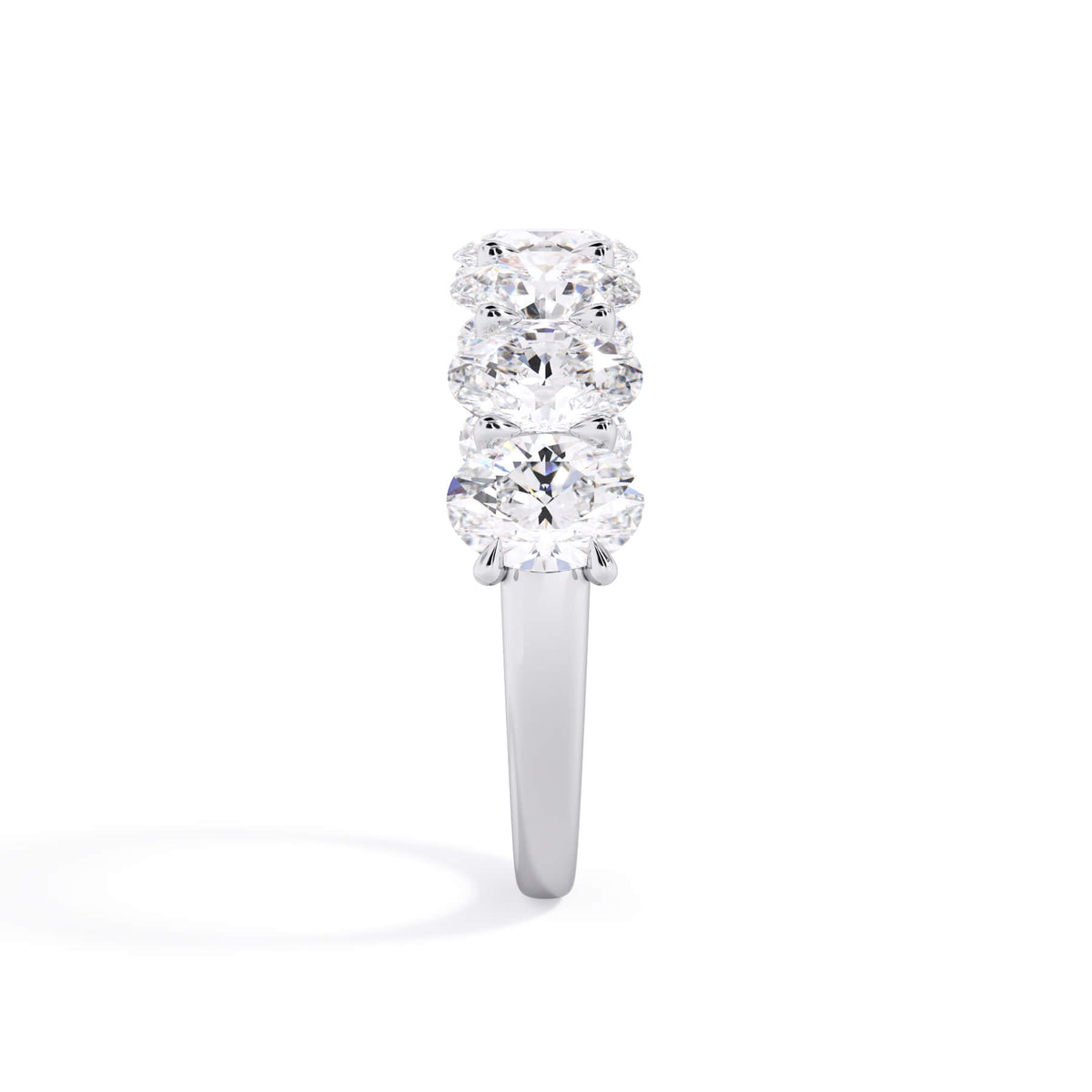 A picture of a seven stone diamond wedding ring with oval shaped diamonds that are U prong set in white gold or platinum on a white background with a side profile view.