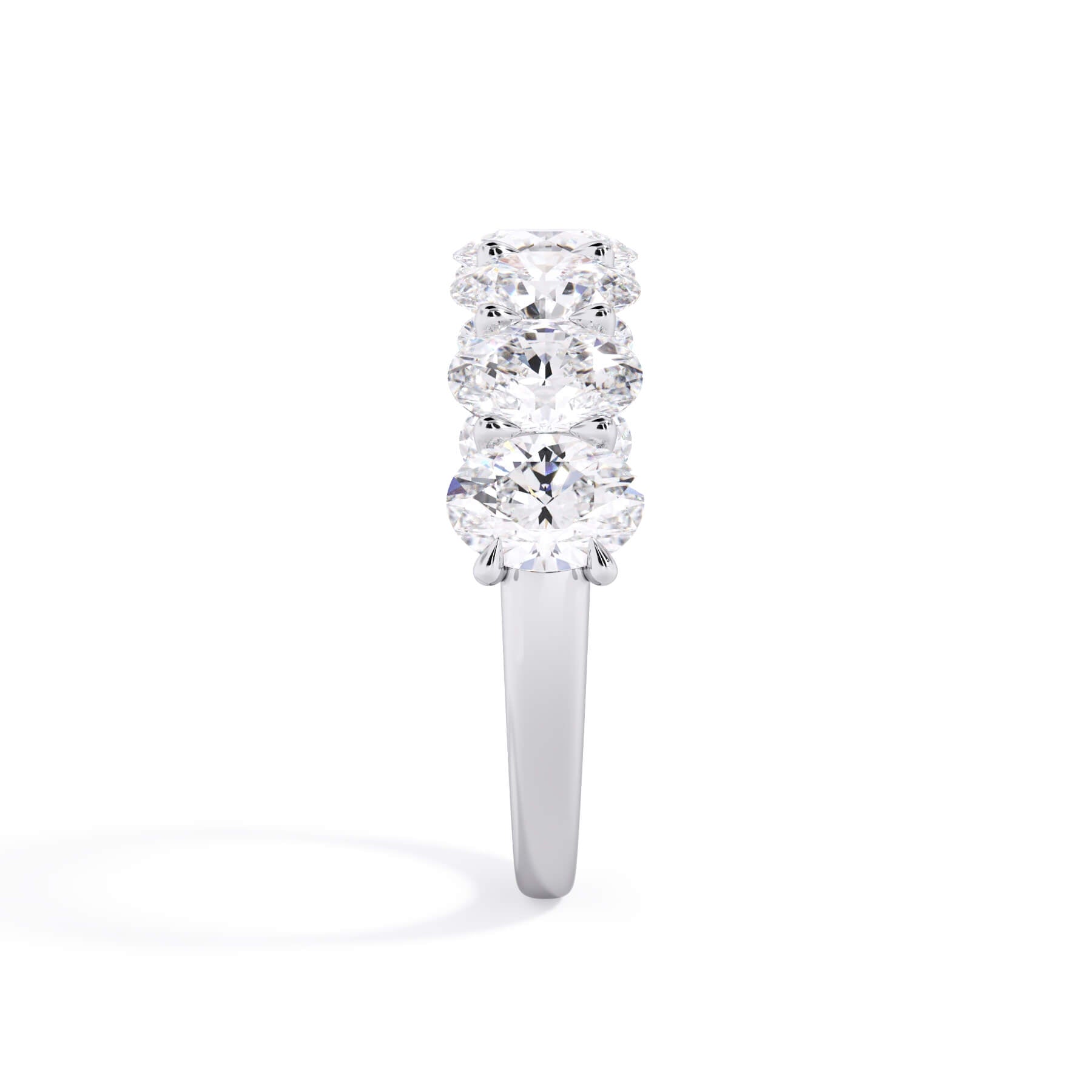 A picture of a seven stone diamond wedding ring with oval shaped diamonds that are U prong set in white gold or platinum on a white background with a side profile view.