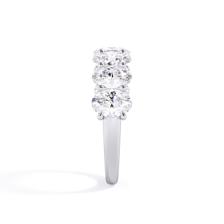 A picture of a seven stone diamond wedding ring with oval shaped diamonds that are U prong set in white gold or platinum on a white background with a side profile view.