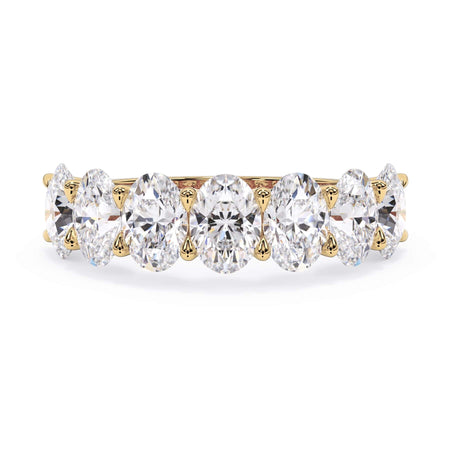 A picture of a seven stone diamond wedding ring with oval shaped diamonds that are U prong set in yellow gold on a white background with the ring facing forward, lying down.