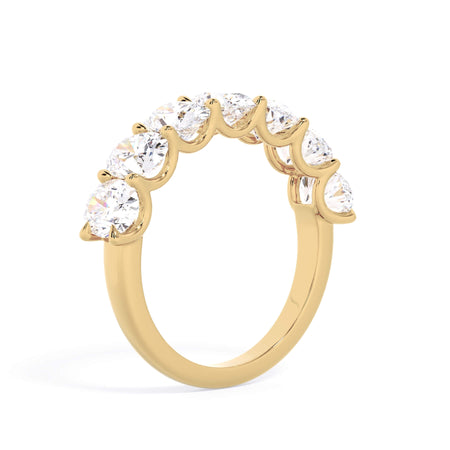 A picture of a seven stone diamond wedding ring with oval shaped diamonds that are U prong set in yellow gold on a white background with a slightly angled, through the finger view.