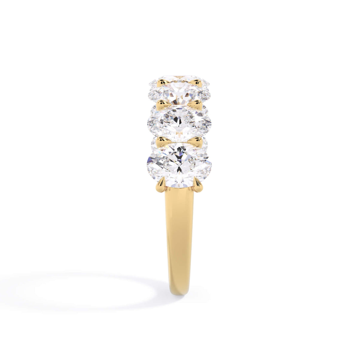 A picture of a seven stone diamond wedding ring with oval shaped diamonds that are U prong set in yellow gold on a white background with a side profile view.
