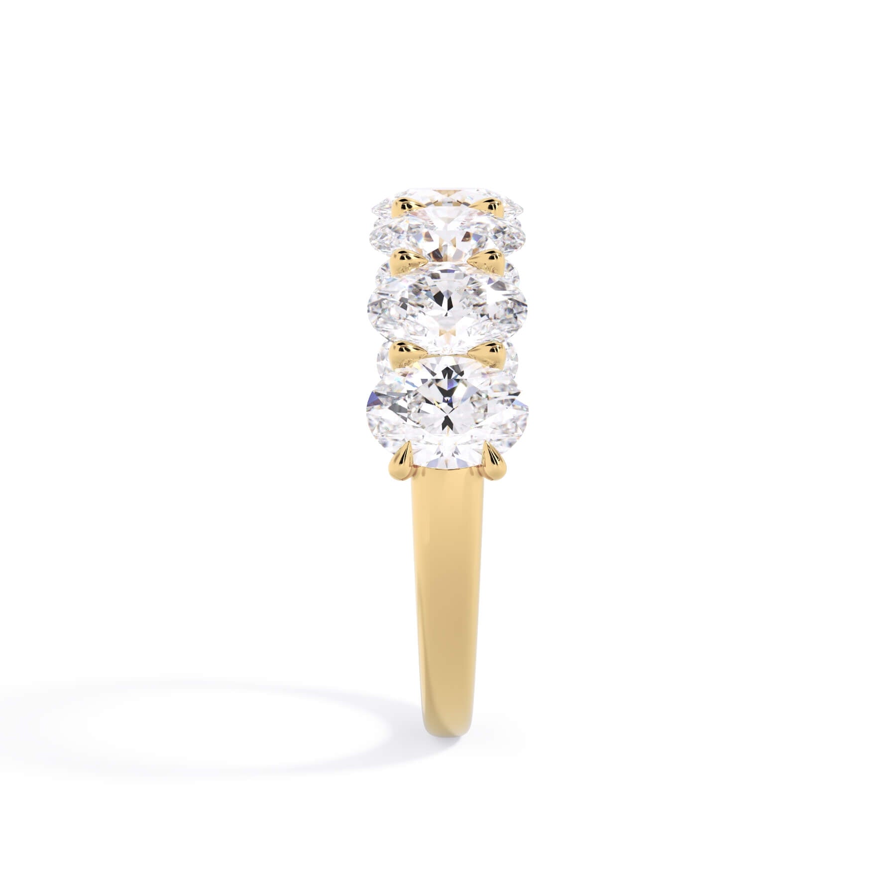 A picture of a seven stone diamond wedding ring with oval shaped diamonds that are U prong set in yellow gold on a white background with a side profile view.