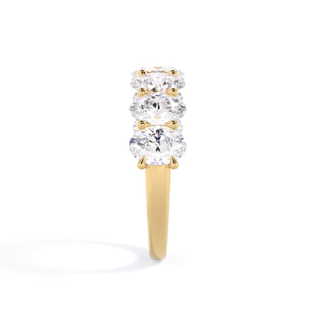A picture of a seven stone diamond wedding ring with oval shaped diamonds that are U prong set in yellow gold on a white background with a side profile view.