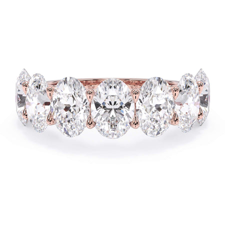A picture of a seven stone diamond wedding ring with oval shaped diamonds that are U prong set in rose gold on a white background with the ring facing forward, lying down.