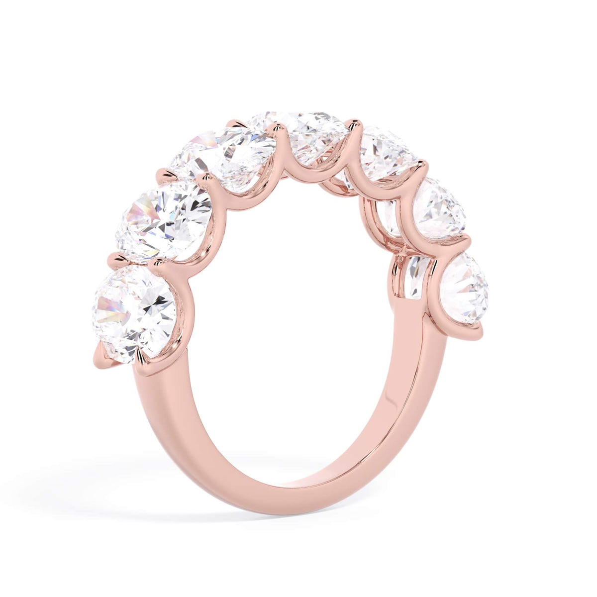 A picture of a seven stone diamond wedding ring with oval shaped diamonds that are U prong set in rose gold on a white background with a slightly angled, through the finger view.