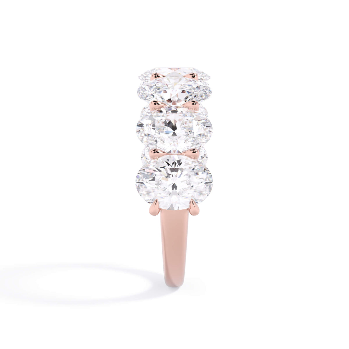A picture of a seven stone diamond wedding ring with oval shaped diamonds that are U prong set in rose gold on a white background with a side profile view.