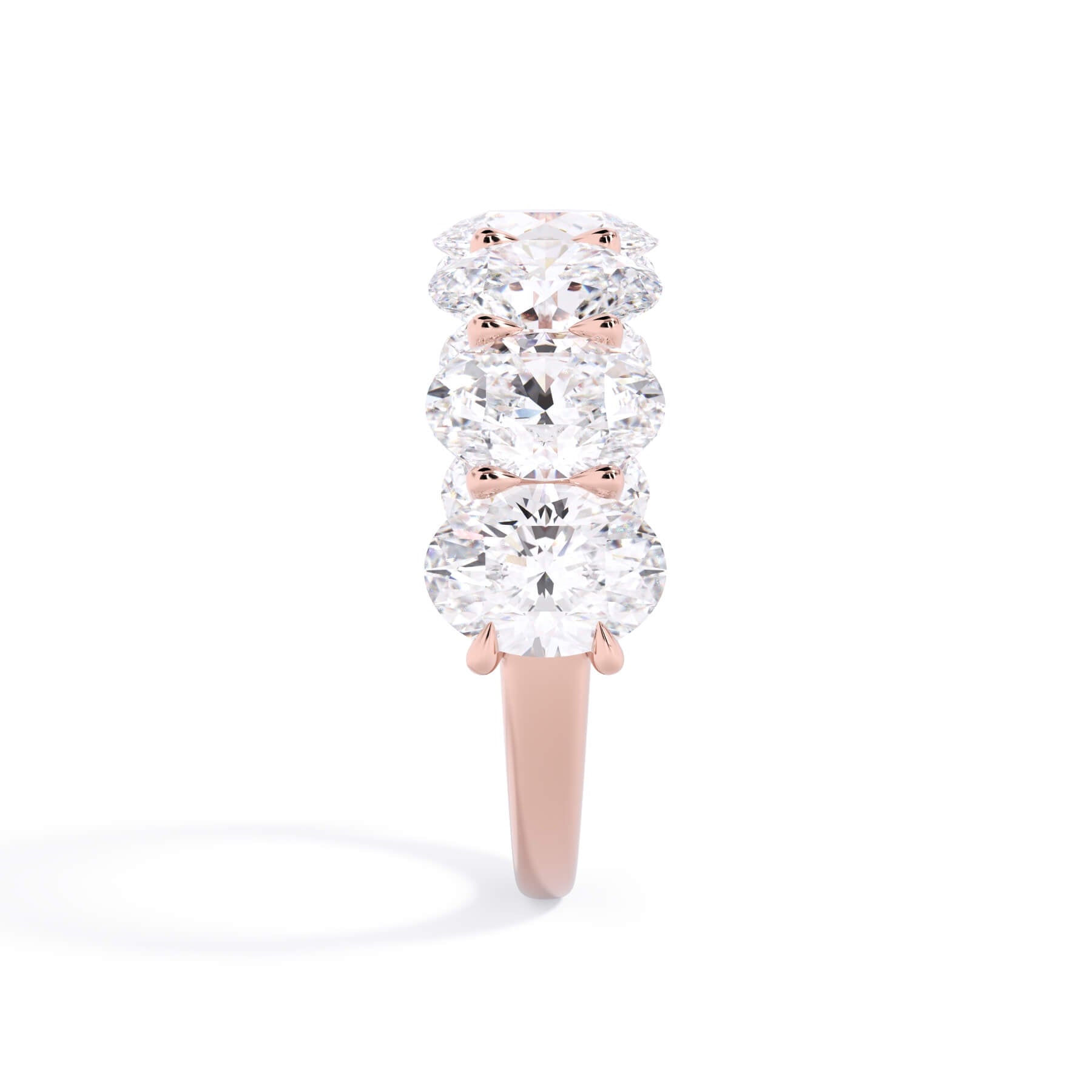 A picture of a seven stone diamond wedding ring with oval shaped diamonds that are U prong set in rose gold on a white background with a side profile view.
